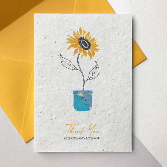 Photo of a Thank You for Helping Me Grow plantable wildflower seed card in yellow. The card has a pen and watercolour sunflower design. Text reads Thank You For Helping Me Grow. The card comes with a yellow eucalyptus paper envelope.
