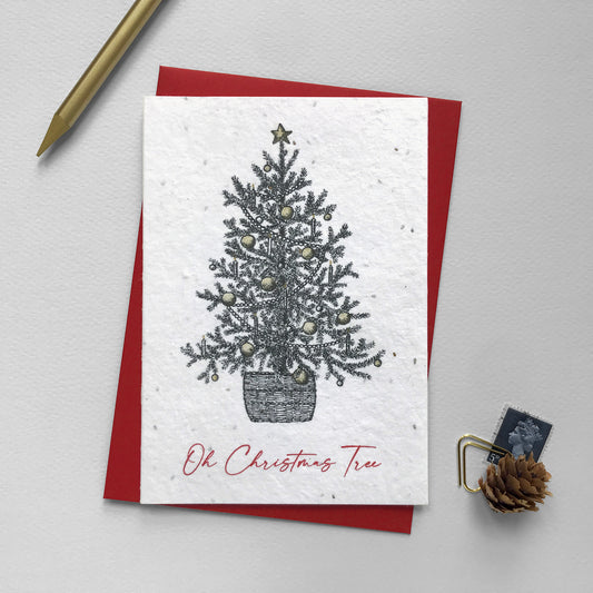 Image shows an A6 plantable Christmas Illustration card featuring pen illustrated Christmas Tree. The baubles and star on top are hand finished using a gold pencil. The red text underneath reads 'Oh Christmas Tree'. This recycled, biodegradable card is embedded with seeds so it can be planted to grow beautiful flowers for the garden. Each card comes with a recycled red envelope.
