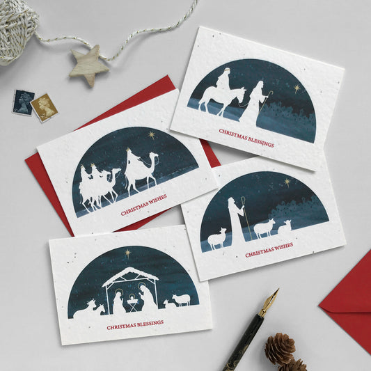 Image shows a pack of 4 Bloom Cards plantable Christmas Nativity cards. Cards feature blue watercolour designs with white silhouettes of Mary and Joseph, a shepherd and flock, three wise men riding camels and the nativity scene. Each card is hand finished with gold pencil details. Text underneath reads 'Christmas Wishes' and 'Christmas Blessings'. Printed onto recycled paper embedded with seeds so you can plant your card and grow Wildflowers. Cards are blank inside and come with red recycled envelopes.