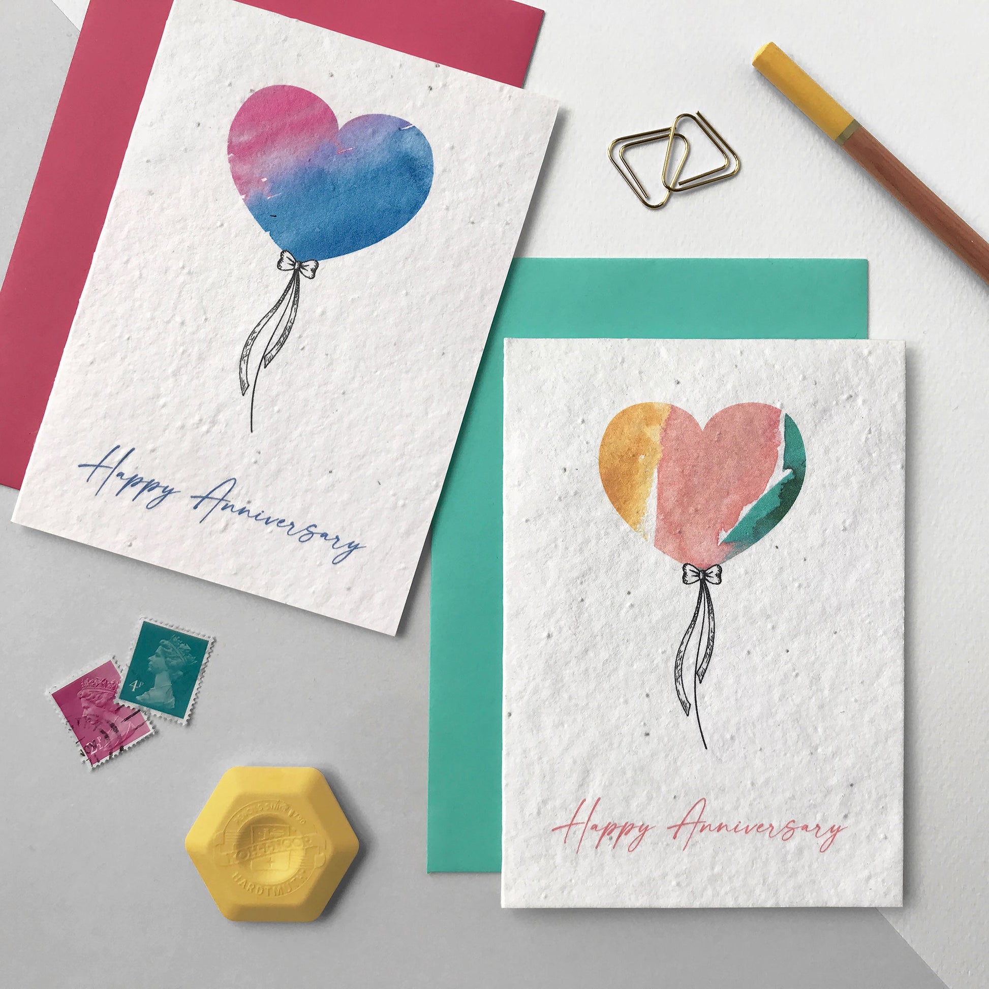 Image shows two Bloom Cards A6 plantable anniversary cards in grey and mint. The cards feature a hand illustrated watercolour and pen heart balloon design. The text underneath reads 'Happy Anniversary'. Printed onto recycled cotton paper and embedded with Wildflower seeds. Each card is blank inside and comes with matching fsc certified eucalyptus paper envelope. Lovingly handmade in Lancashire by Suzanne Marie Paperie.