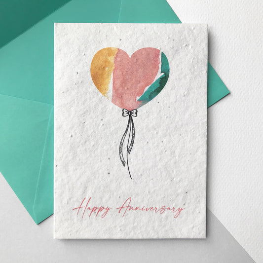Image of a Bloom Cards A6 plantable anniversary card featuring a hand illustrated heart shape balloon design. Watercolour washes in coral, mint and yellow are used to create a colourful balloon with a pen drawn bow and string. The coral pink text underneath reads 'Happy Anniversary'. Printed onto eco-friendly paper made from recycled cotton and embedded with wildflower seeds. The card comes with a matching mint fsc certified eucalyptus envelope.