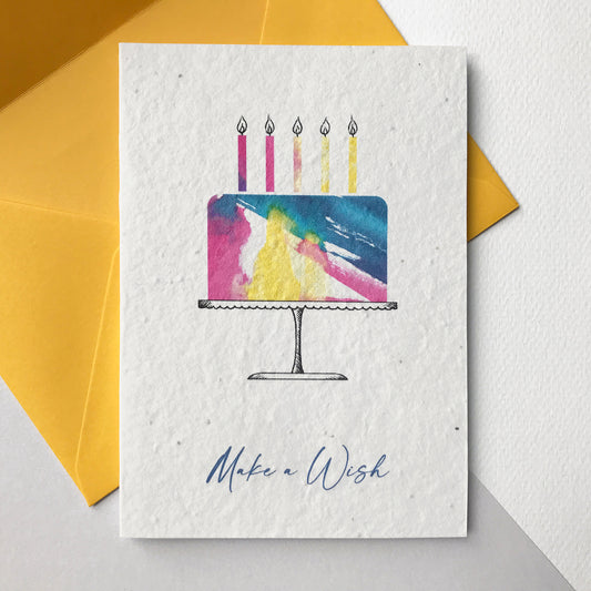 This Bloom Cards A6 plantable birthday card features a hand illustrated watercolour and pen illustration of a cake and candles in washes of blue, yellow and pink. The blue text underneath reads 'Make a Wish'. The card is blank inside and comes with a yellow fsc certified eucalyptus paper envelope. Plant this card and grow a beautiful bee friendly mix of wildflowers for the garden. Lovingly made by Suzanne Marie Paperie.