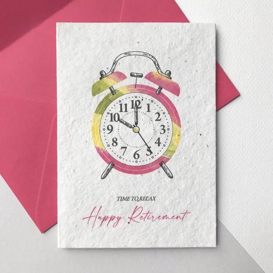 Image shows a Bloom Cards plantable seed paper retirement card featuring a pink and yellow alarm clock hand illustrated using watercolour and pen. The text underneath reads 'time to relax, happy retirement'. The card comes with a magenta pink fsc certified eucalyptus envelope. Printed onto recycled cotton paper embedded with bee friendly wildflower seeds. Lovingly handmade by Suzanne Marie Paperie.