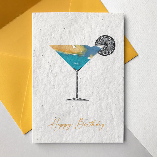 Image shows a Bloom Cards A6 plantable birthday card with a hand illustrated cocktail design. Watercolour washes in yellow and turquoise make up a colourful cocktail with a pen illustrated stem and slice of lemon. The yellow text underneath reads 'Happy Birthday'. Each recycled cotton card is embedded with wildflower seeds, so the card can be planted to grow bee friendly flowers for the garden or pots. The card is blank inside and comes with a yellow fsc certified eucalyptus envelope.