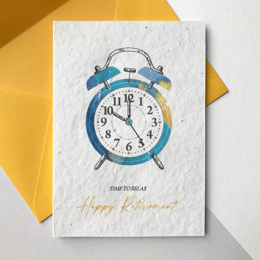 Image shows a Bloom Cards plantable seed paper retirement card featuring a turquoise and yellow alarm clock hand illustrated using watercolour and pen. The text underneath reads 'time to relax, happy retirement'. The card comes with a yellow fsc certified eucalyptus envelope. Printed onto recycled cotton paper embedded with wildflowers seeds. Illustrated and printed in Lancashire by Suzanne Marie Paperie.