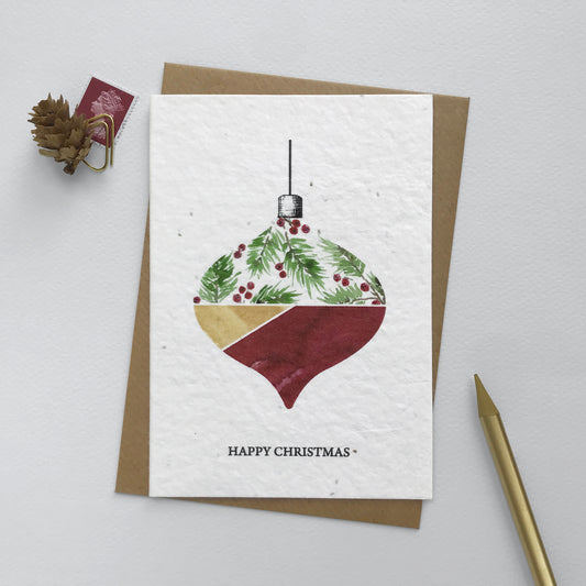 Image shows an A6 Bloom Cards plantable Christmas card featuring a hand illustrated  bauble with a fir and berries design. The berries have been hand finished with Bio-glitter Pure. This plastic free glitter is proven to biodegrade in the natural environment in around 4 weeks. The black text underneath reads 'Happy Christmas'. Printed onto recycled paper embedded with Wildflower seeds, simply plant the card to grow beautiful flowers for the garden. Comes with a recycled kraft envelope.