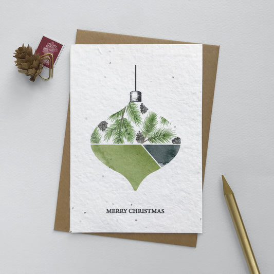 Image shows an A6 Bloom Cards plantable Christmas card featuring a hand illustrated  bauble with a pine needles and cones design. The pine cones have been hand finished with Bio-glitter Pure. This plastic free glitter is proven to biodegrade in the natural environment in around 4 weeks. The black text underneath reads 'Merry Christmas'. Printed onto recycled paper embedded with Wildflower seeds, simply plant the card to grow beautiful Wildflowers for the garden. Comes with a recycled kraft envelope.