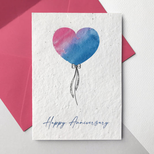 Image of a Bloom Cards A6 plantable anniversary card featuring a hand illustrated heart shape balloon design. Watercolour washes in magenta and blue are used to create a colourful balloon with a pen drawn bow and string. The blue text underneath reads 'Happy Anniversary'. Printed onto eco-friendly paper made from recycled cotton and embedded with wildflower seeds. The card comes with a matching mint fsc certified eucalyptus envelope.