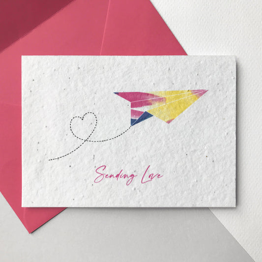 Image of a Bloom Cards A6 plantable note card featuring a hand illustrated design. Watercolour washes in magenta, blue and yellow are used to create this modern paper plane design with a pen drawn heart trail. The magenta pink text underneath reads 'Sending Love'. This recycled cotton card is printed onto wildflower seed paper, so your recipient can grow their card and enjoy some beautiful flowers. The card comes with a matching magenta fsc certified eucalyptus envelope.