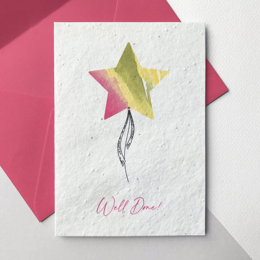 Image shows a Bloom Cards A6 plantable card featuring a brightly coloured pink, yellow and green watercolour star shape balloon with a pen drawn ribbon. The pink text underneath reads 'Well Done!'. The hand illustrated design is printed onto eco-friendly recycled cotton paper embedded with seeds so that it can be planted to grow bee friendly wildflowers. The card is blank inside and comes with a matching magenta pink fsc certified eucalyptus paper envelope. Handmade by Suzanne Marie Paperie.