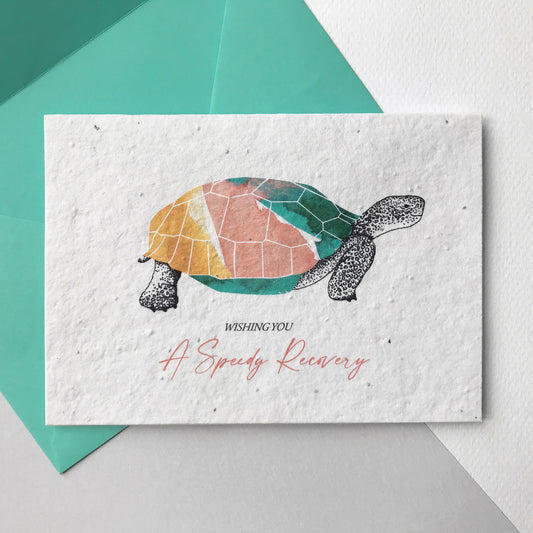 Image of a Bloom Cards plantable speedy recovery card featuring a hand illustrated tortoise design. This cheerful tortoise has a colourful coral, mint and yellow shell and pen drawn head, legs and tail. The coral pink text underneath reads 'Wishing You A Speedy Recovery'. This 100% recycled card is printed onto wildflower seed paper so your recipient can grow their card and enjoy some beautiful flowers. The card comes with a mint green fsc certified eucalyptus envelope.
