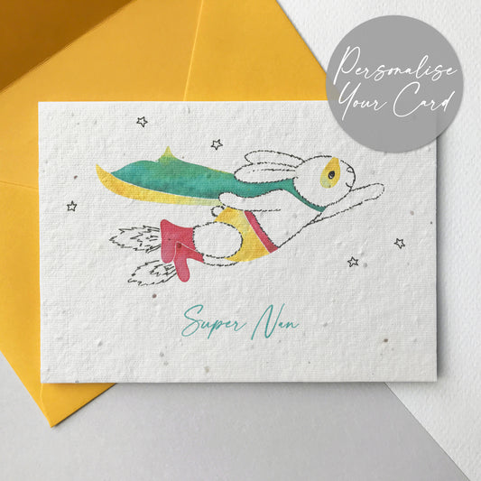 A photo of a hand illustrated Super Nan plantable wildflower seed card in yellow. A pen drawn bunny is flying through the stars wearing a watercolour painted turquoise and yellow cape, yellow mask and pants, red belt and red rocket boots. The turquoise personalised text underneath reads Super Nanny. The card comes with a yellow fsc certified eucalyptus paper envelope.