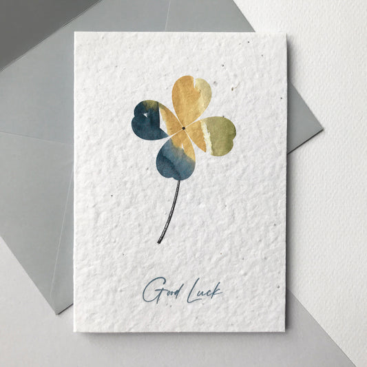 Image shows a Bloom Cards A6 plantable card with a grey, natural and green watercolour and pen four leaf clover design. The grey text underneath reads 'Good Luck'. Hand illustrated and printed onto plantable wildflower seed paper, so the card can be planted to grow a beautiful mix of rudbeckia, sweet alyssum, baby's breath and poppies. The card is blank inside and comes with a grey fsc certified eucalyptus paper envelope. Lovingly illustrated and printed by Suzanne Marie Paperie.